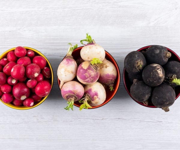 Top view fresh different color radishes in three black bowls on white wooden background. horizontal copy space for text